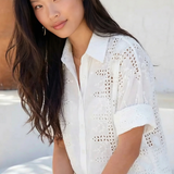 Woman wearing a white lace top and shorts sitting outdoors.