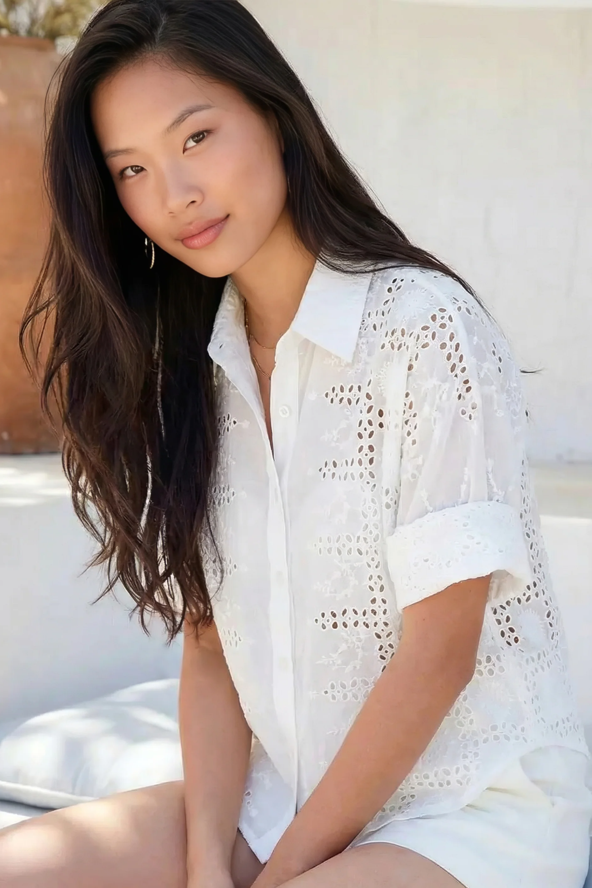 Woman wearing a white lace top and shorts sitting outdoors.