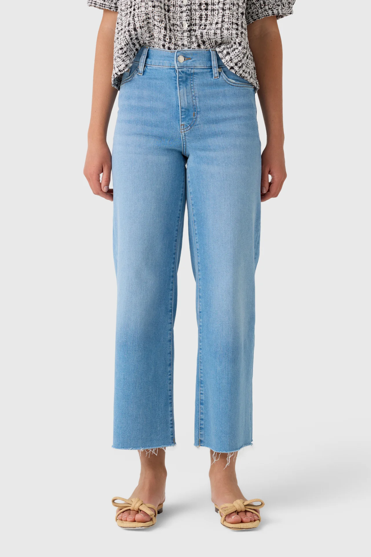 A model wearing light blue cropped jeans with a straight-leg fit, paired with a patterned top and beige sandals, shown from the waist down on a light gray background.