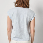 Woman wearing a light blue t-shirt and white pants against a plain background
