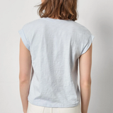 Woman wearing a light blue t-shirt and white pants against a plain background