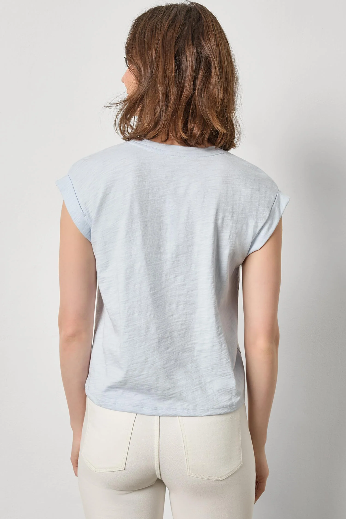 Woman wearing a light blue t-shirt and white pants against a plain background