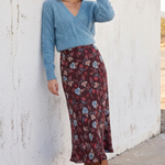 Model wearing floral skirt and blue top on a white background