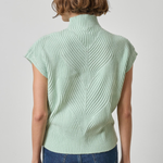 A woman viewed from the back wearing a pale mint green ribbed knit mock-neck top with short sleeves and blue jeans, against a light gray studio background.