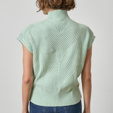 A woman viewed from the back wearing a pale mint green ribbed knit mock-neck top with short sleeves and blue jeans, against a light gray studio background.