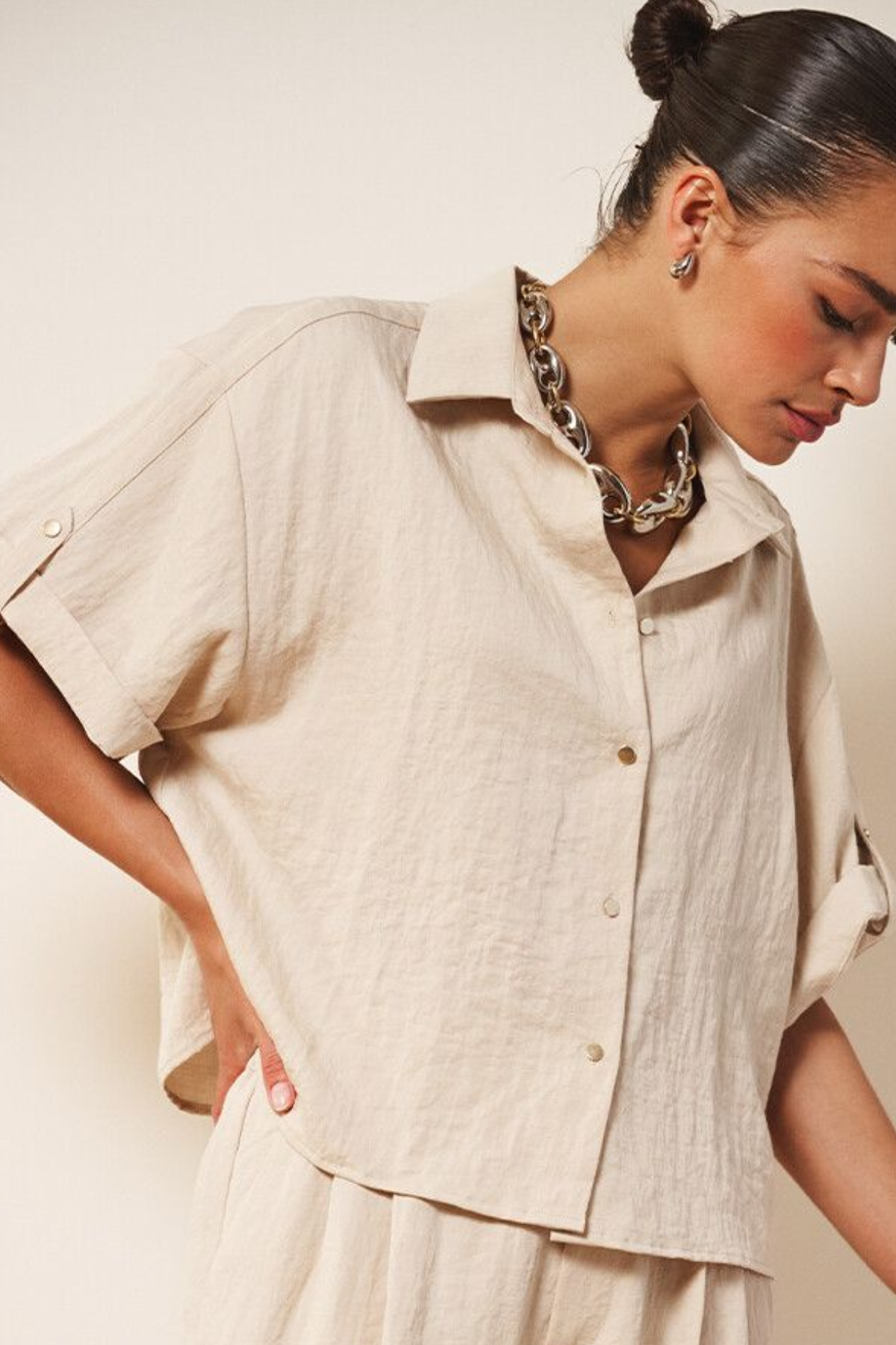 Woman wearing a beige button-up shirt and pants against a plain background