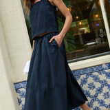 Woman wearing a navy blue sleeveless top and skirt standing in front of a building with decorative tiles.