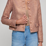 Person wearing a brown textured jacket and blue jeans on a plain background