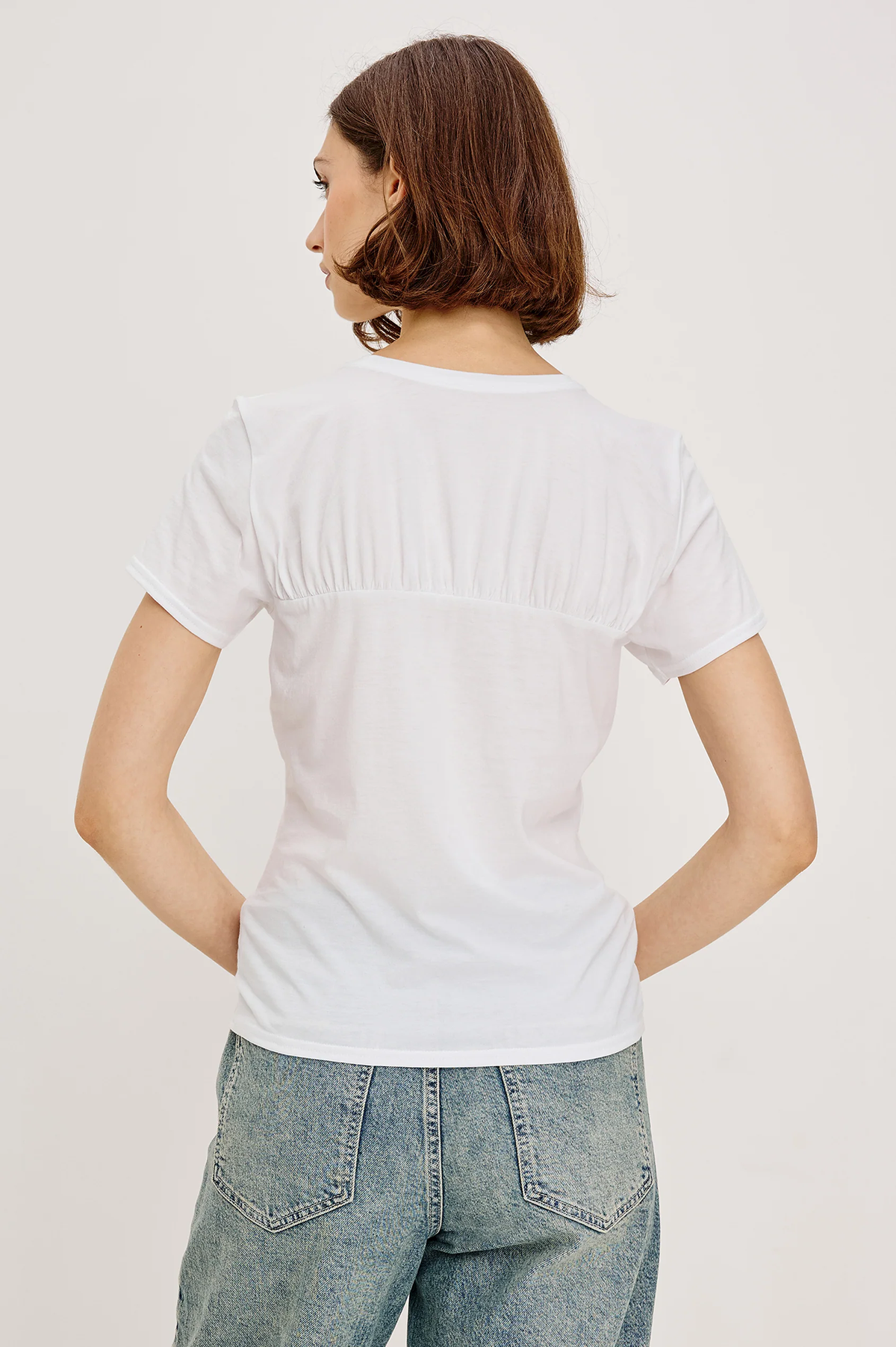 Person wearing a plain white t-shirt and jeans on a light background