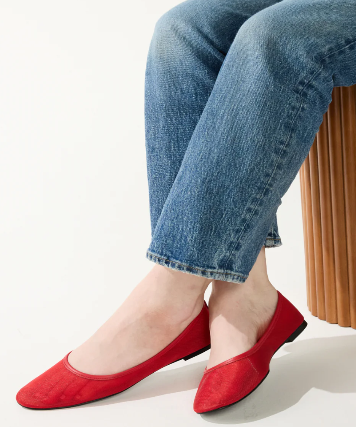 Person wearing red flat shoes and blue jeans sitting on a white background