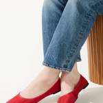 Person wearing red flat shoes and blue jeans sitting on a white background