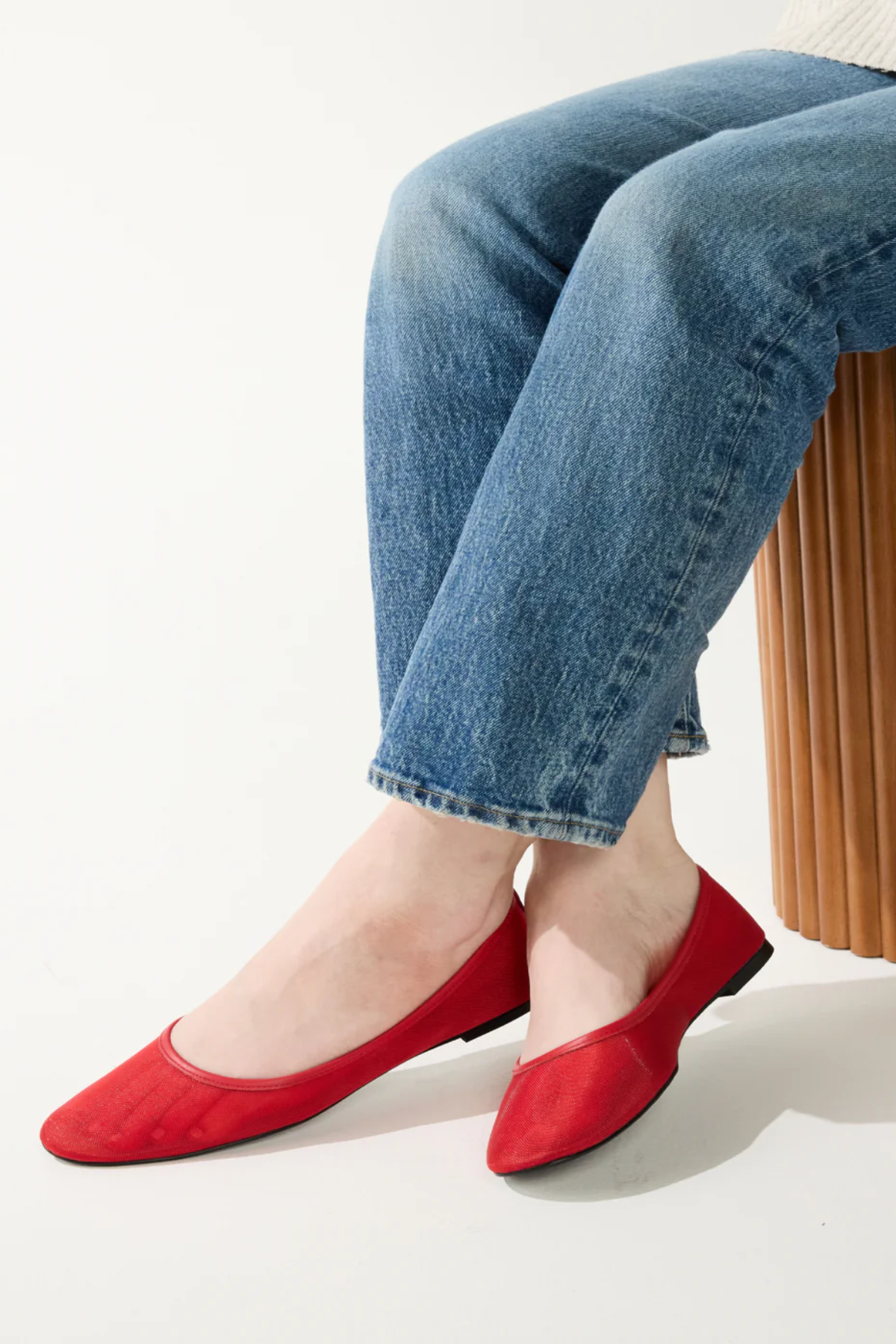 Person wearing red flat shoes and blue jeans sitting on a white background