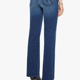 Rear view of a model wearing blue denim jeans with a distinctive 'M' logo on the back pocket, paired with black high-heeled boots against a light gray background.