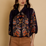 Woman wearing a dark floral embroidered blouse against a beige background