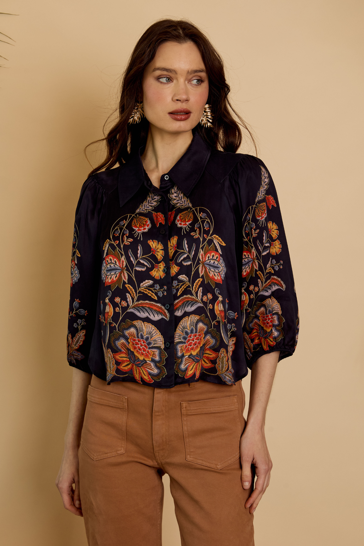 Woman wearing a dark floral embroidered blouse against a beige background