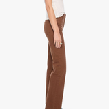 A side-profile view of a model wearing brown wide-leg pants, a white sleeveless top, and green snakeskin-patterned boots against a plain white background.