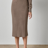 A model wearing a taupe brown ribbed knit midi skirt and matching knit top, paired with beige strappy heels, against a neutral studio backdrop.