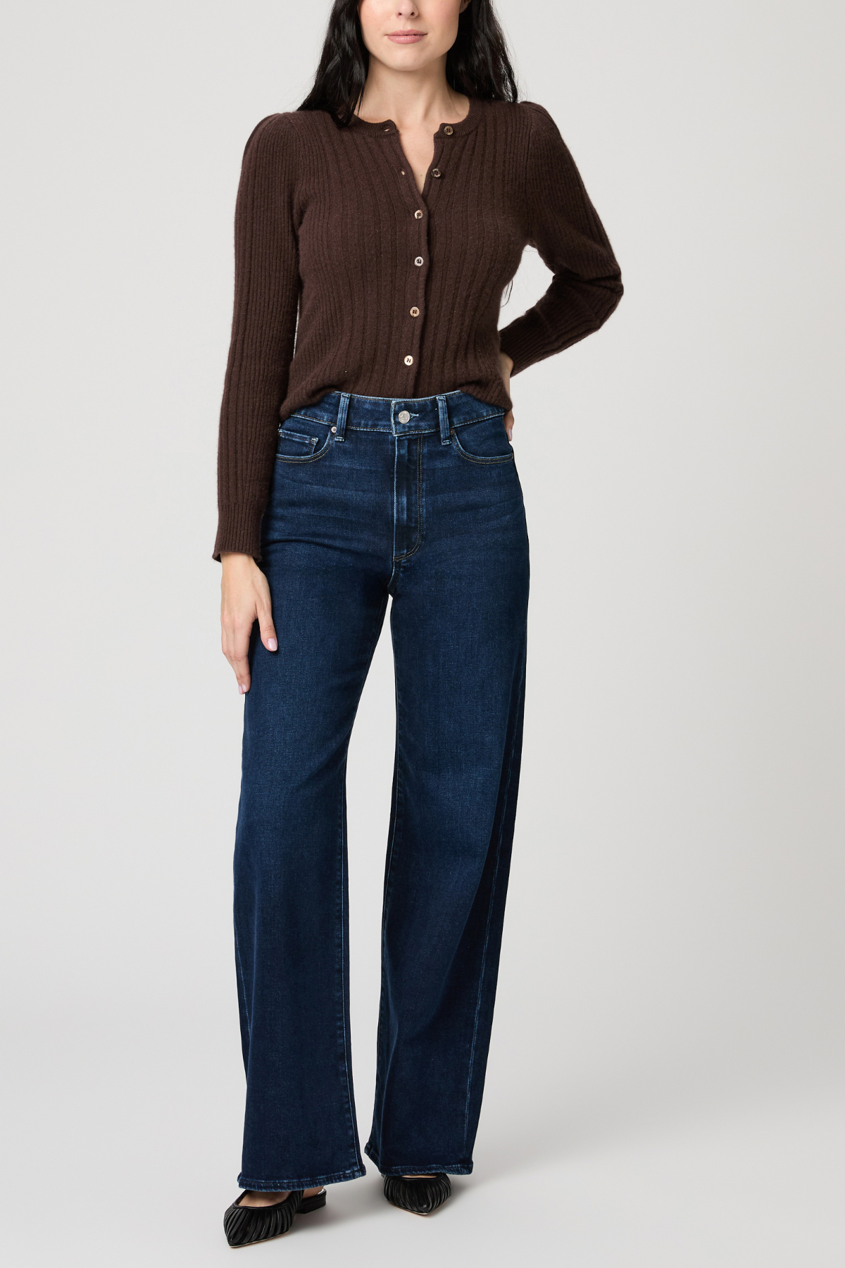 Woman wearing a brown ribbed sweater and blue jeans on a white background