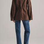 A model shown from the back wearing a brown corduroy jacket with a drawstring waist and blue jeans, against a light gray studio background.
