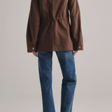 A model shown from the back wearing a brown corduroy jacket with a drawstring waist and blue jeans, against a light gray studio background.