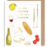 A white greeting card with gold text reading 'to the HOSTESS with the MOSTESS' and illustrated food and drink motifs, shown with a brown kraft envelope behind it on a white background.
