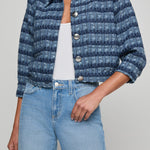 Person wearing a blue patterned jacket and light blue jeans on a gray background