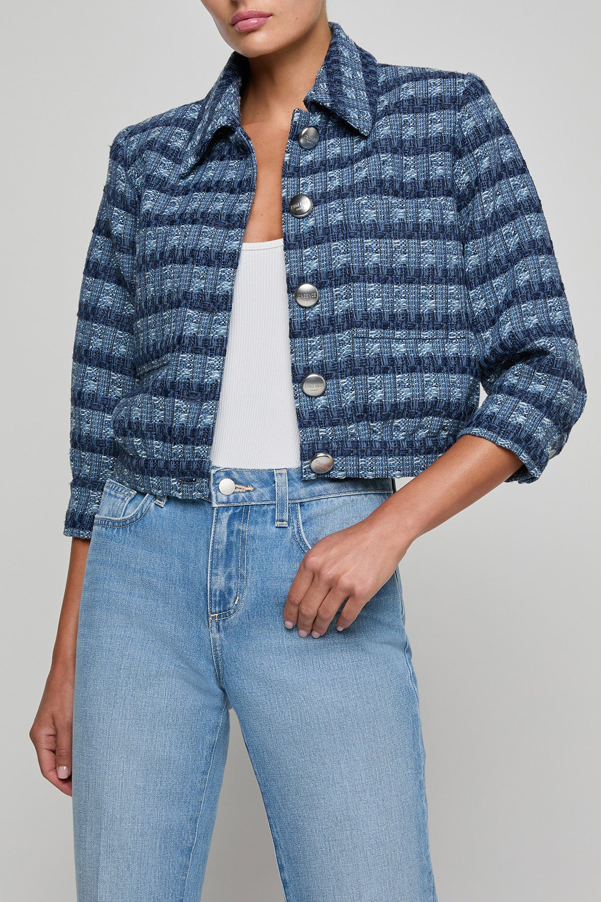 Person wearing a blue patterned jacket and light blue jeans on a gray background