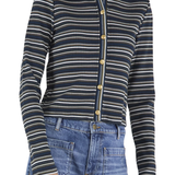 A woman wearing a navy blue ribbed knit cardigan with thin cream and white horizontal stripes, featuring gold buttons down the front, paired with blue jeans.