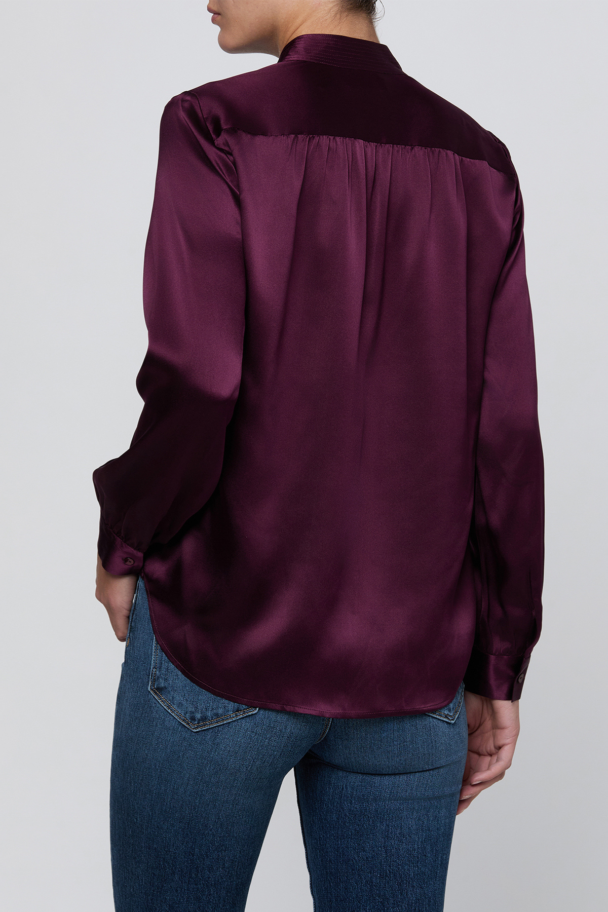 A woman wearing a deep purple satin blouse with a contrasting velvet collar and shoulders, paired with blue jeans, shown from the back against a light gray background.