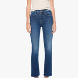 A model wearing a pair of medium-wash blue cropped flare jeans, paired with a cream-colored short-sleeve top and metallic silver high-heeled sandals, set against a plain light gray background.