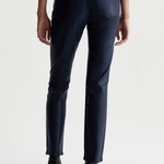 Rear view of a model wearing dark navy blue slim-fit jeans and black ankle boots against a light gray studio background.
