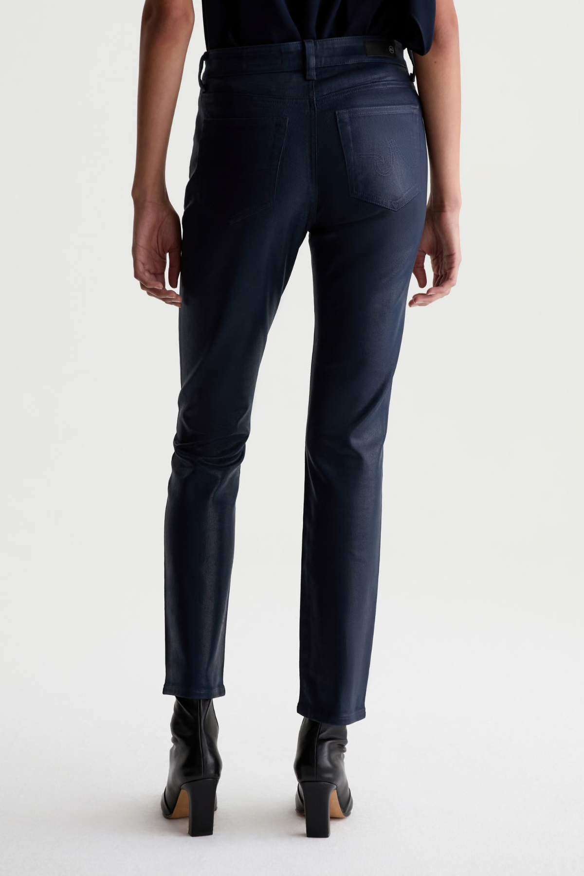 Rear view of a model wearing dark navy blue slim-fit jeans and black ankle boots against a light gray studio background.