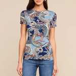 A woman modeling a short-sleeve crewneck t-shirt with a blue and beige paisley pattern, paired with blue jeans, against a solid beige background.