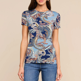 A woman modeling a short-sleeve crewneck t-shirt with a blue and beige paisley pattern, paired with blue jeans, against a solid beige background.