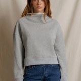 Woman wearing a gray sweater and blue jeans against a beige background