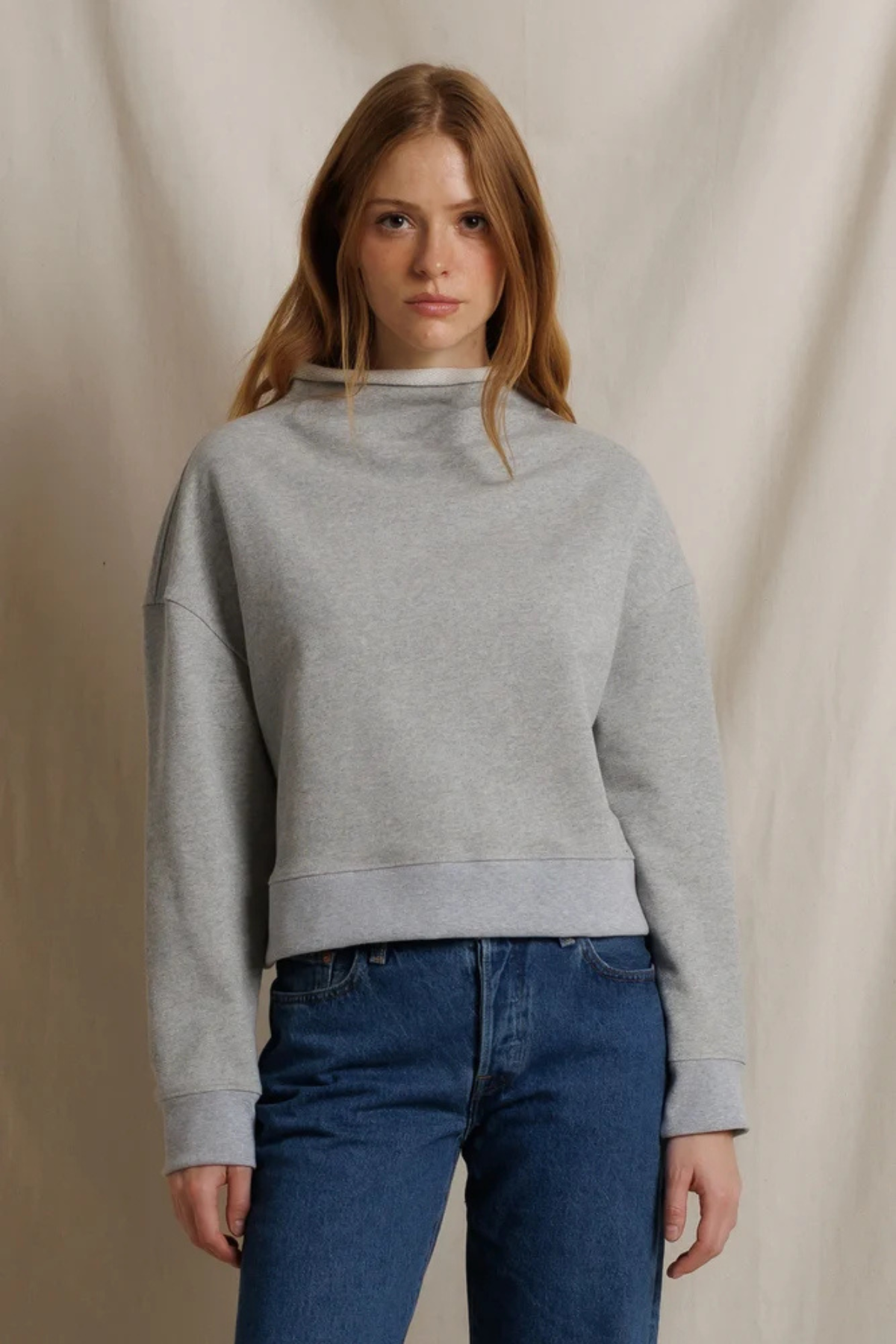 Woman wearing a gray sweater and blue jeans against a beige background