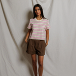 Woman wearing a striped shirt and brown shorts standing against a plain white background