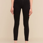 A model wearing black skinny jeans with a black belt featuring a prominent gold buckle, styled with a white top and black heels against a beige background.