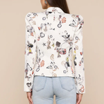 Woman wearing a white blouse with colorful geometric pattern and light blue jeans on a beige background