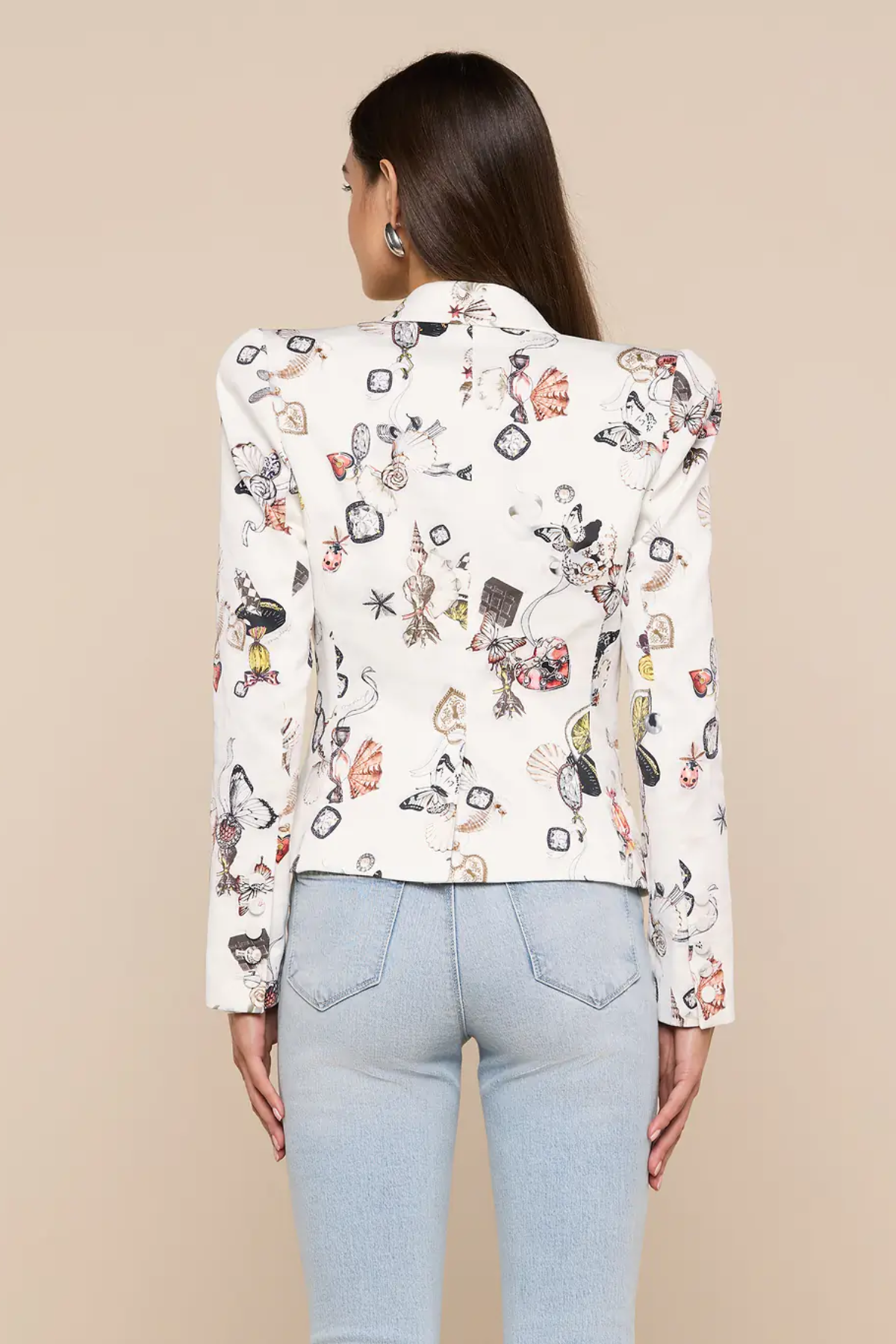 Woman wearing a white blouse with colorful geometric pattern and light blue jeans on a beige background