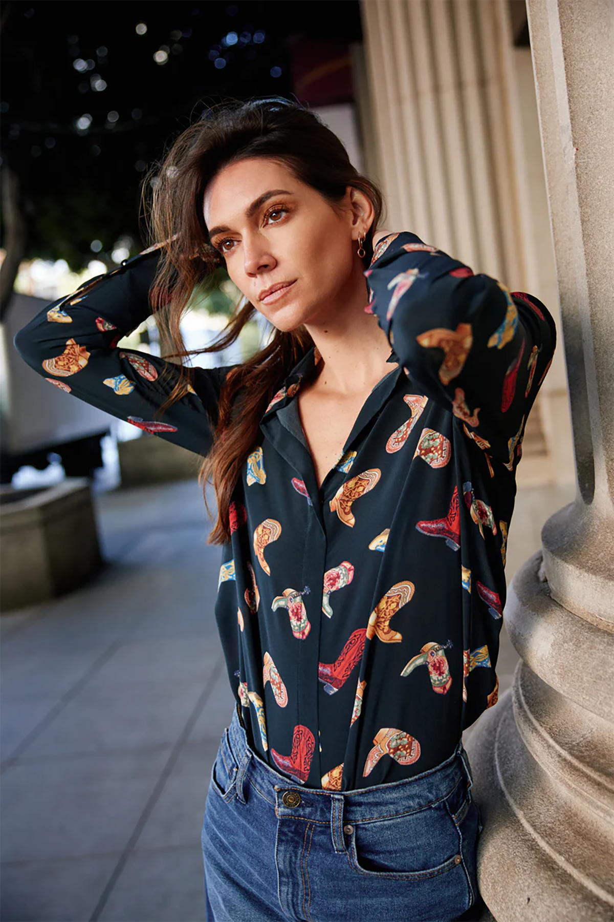 Woman wearing a patterned shirt and jeans standing outdoors.