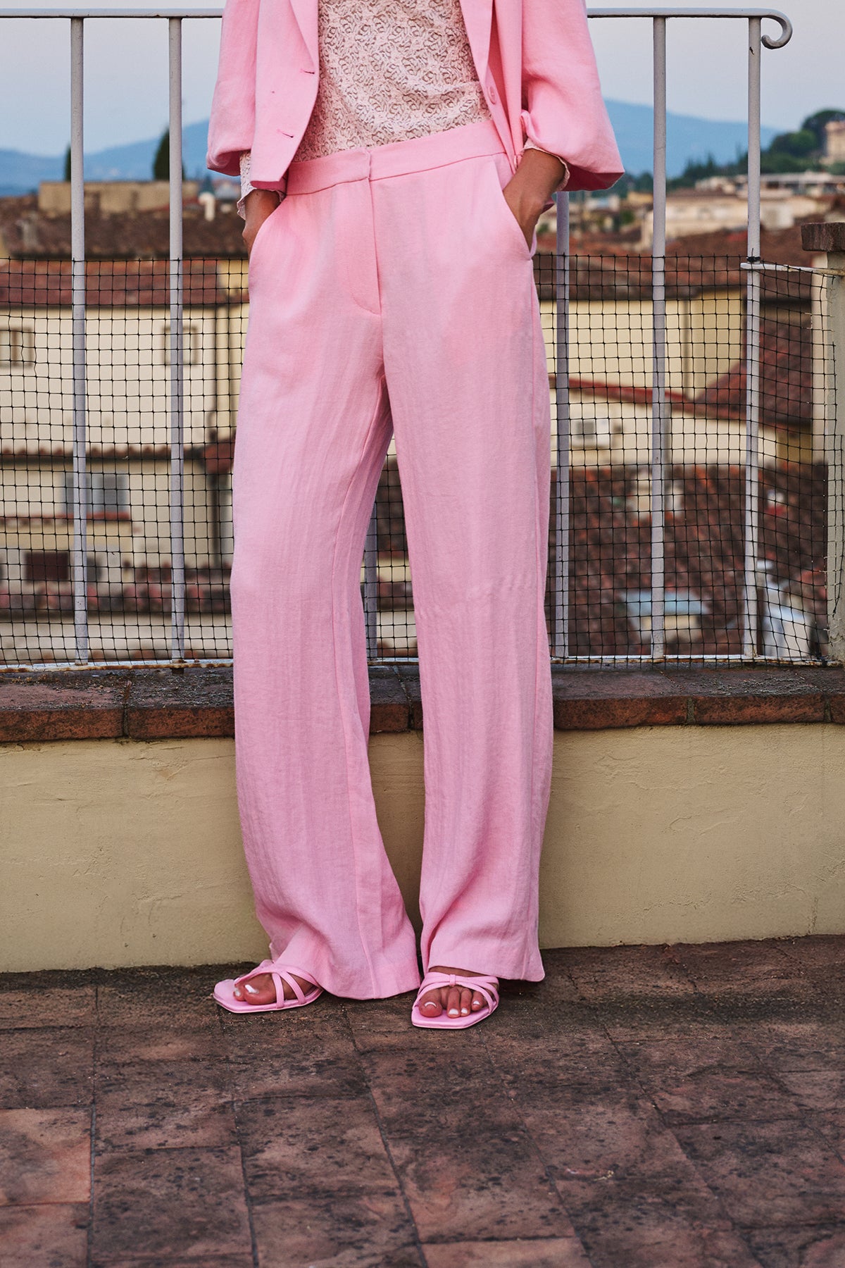 Person wearing a pink suit standing on a rooftop with a scenic background