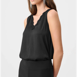 A woman modeling a black sleeveless top with a scalloped V-neckline, paired with black pants, against a light gray studio background.