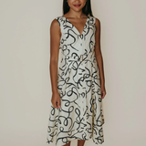 Woman wearing a white dress with black abstract patterns against a plain background