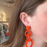 Model wearing bright orange linked drop earrings featuring three open circular shapes in a bold statement design.