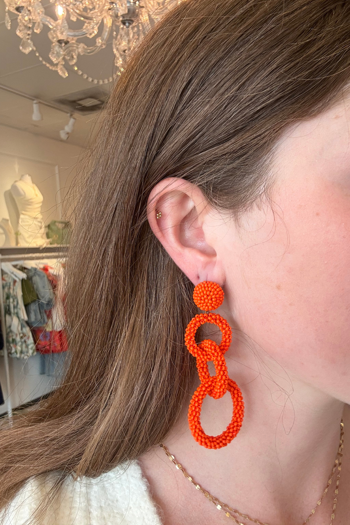 Model wearing bright orange linked drop earrings featuring three open circular shapes in a bold statement design.