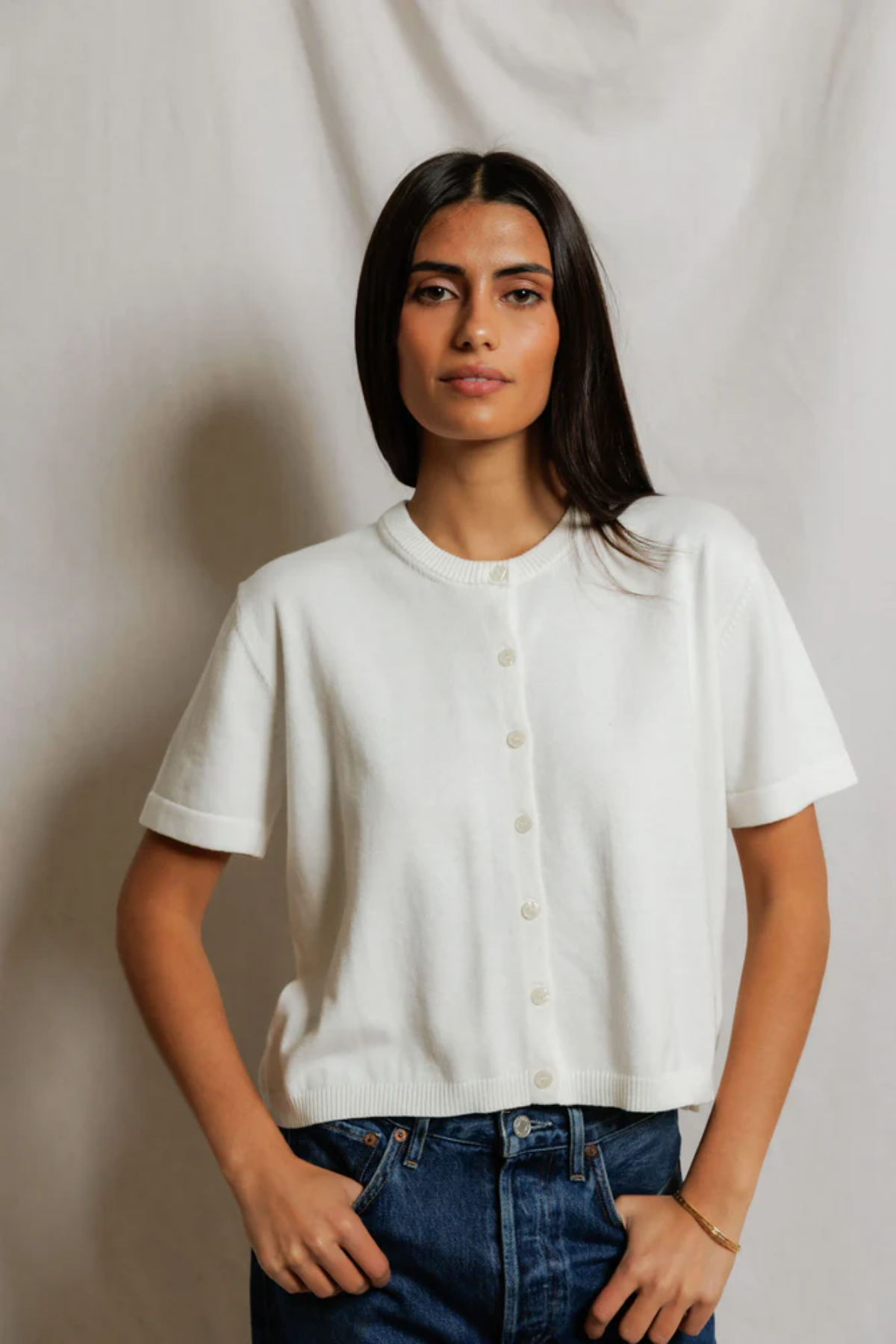 Woman wearing a white shirt and blue jeans against a plain background