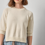 Woman wearing a beige sweater and blue jeans against a plain background