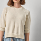 Woman wearing a beige sweater and blue jeans against a plain background