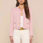 Woman wearing a pink jacket over a white top and beige pants on a beige background